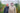 Haley and Finlay from Seeds of Scotland stand inside a polytunnel full of diverse plants, wearing rain jackets and beanies.