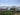 Person facing away from the camera inside large polytunnel full of various crops, in front of vast landscape of hills and sea